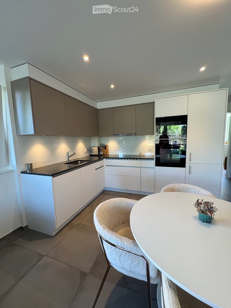 Modern kitchen with white and grey cabinets, a central island, a sink, and a dining area with a round table and two chairs.