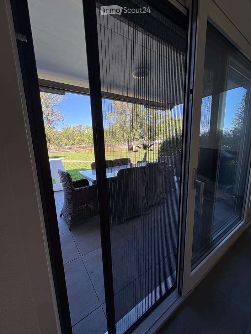 Balcony with large glass sliding doors, tiled floor, and outdoor furniture including a table and chairs.