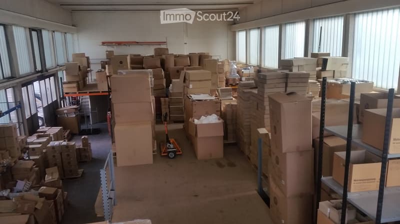 Large, empty warehouse space with numerous cardboard boxes stacked throughout, large windows with blinds, and a forklift in the center.