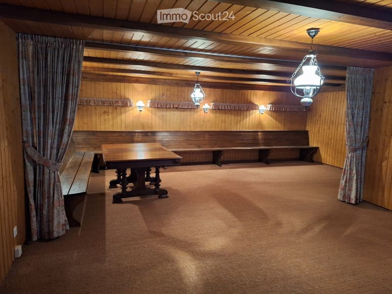 Wooden-paneled room with a central wooden table, benches, and hanging lanterns.