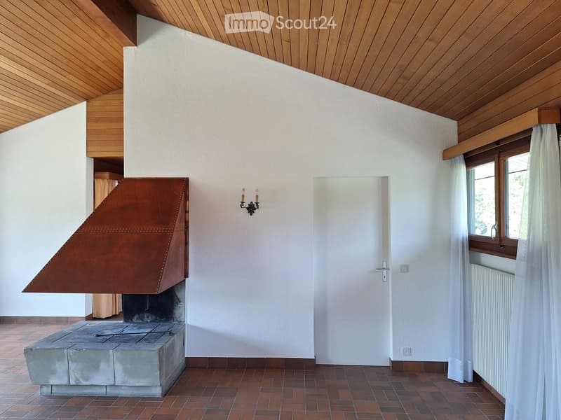 Modern living room with a prominent fireplace, wooden ceiling, tiled floor, and large windows with curtains.