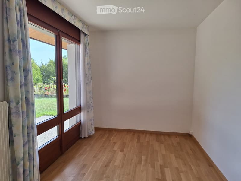 Empty room with wooden flooring, large window with floral curtains, and a radiator on the left side.