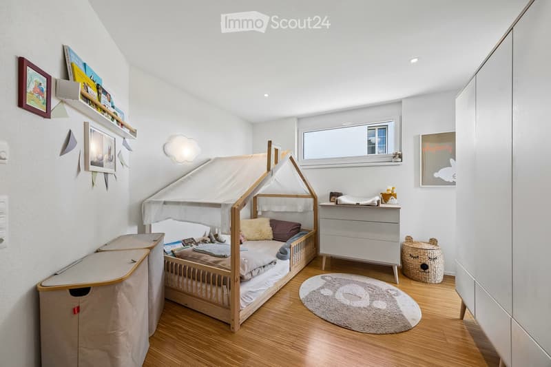 Cozy children's bedroom with a wooden bed under a canopy, a nightstand, a round rug, and shelves with books and decorations.