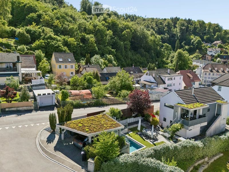 Aerial view of a residential neighborhood with multiple houses, gardens, and a swimming pool in the foreground.
