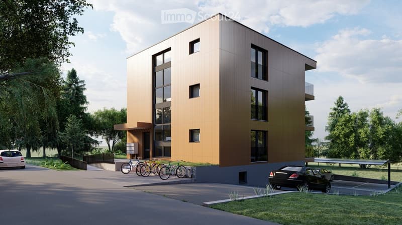 Modern multi-story building with large windows and a balcony, surrounded by greenery and parked cars.