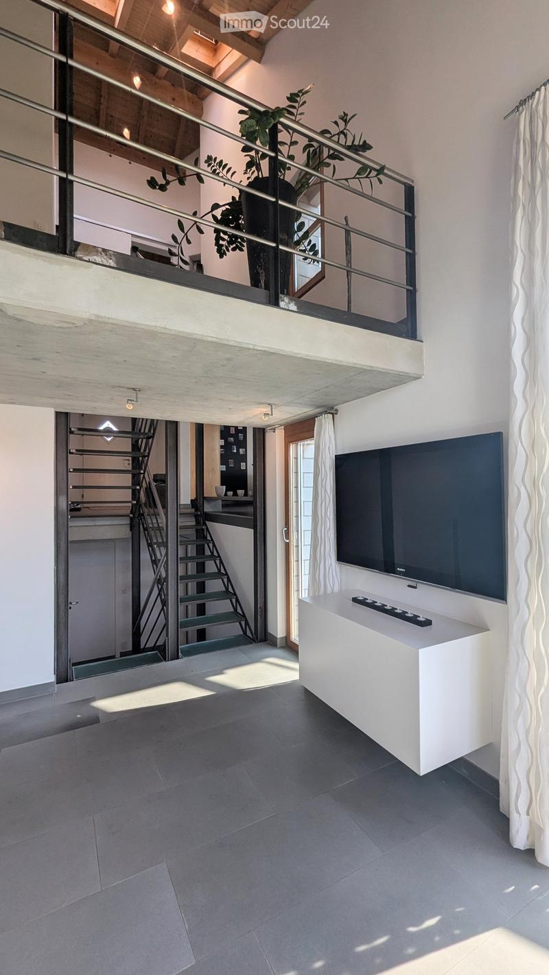 Modern living room with a large flat-screen TV on a white console table, white curtains, and a staircase leading to an upper level with a plant in the corner.