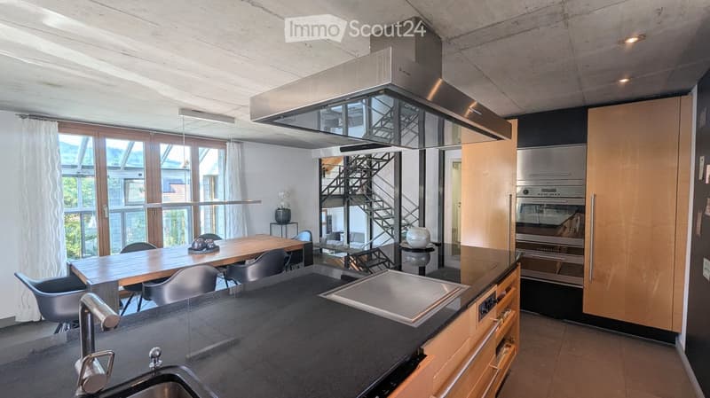 Modern kitchen with a large island, black countertops, wooden dining table, and stainless steel appliances.