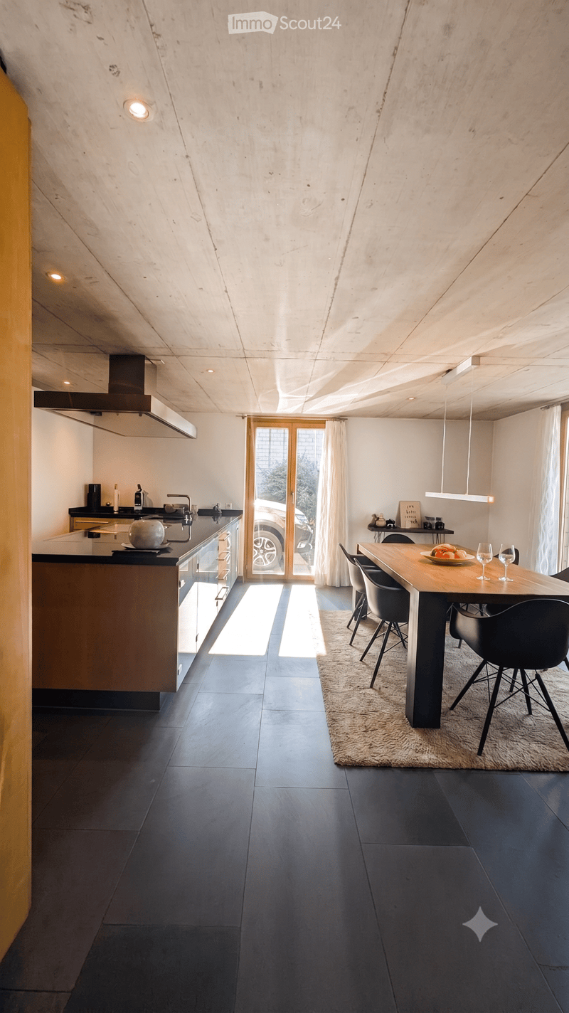 Modern kitchen and dining area with dark tiled flooring, sleek kitchen island, dining table with chairs, and pendant lighting.