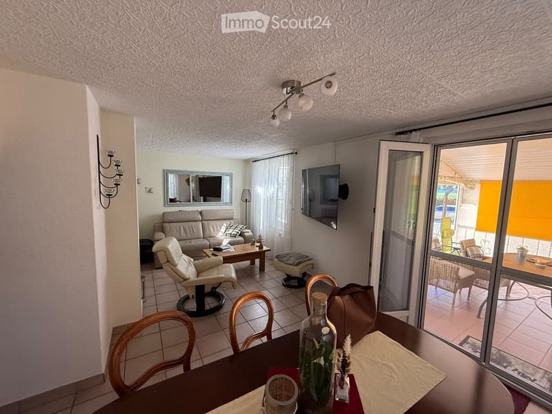 Bright living room with a sofa, coffee table, armchair, dining table, and a large sliding glass door leading to a patio.