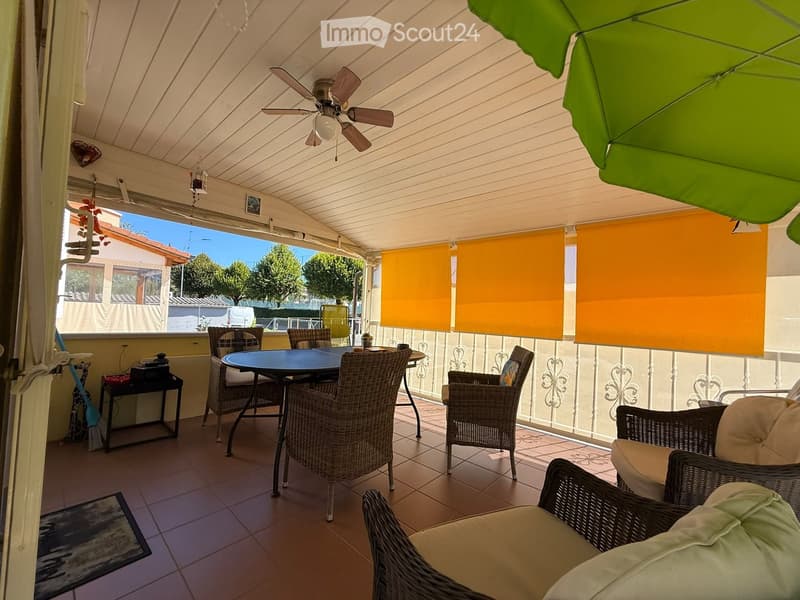 Balcony with a dining table, chairs, and an umbrella, featuring a ceiling fan and orange blinds.
