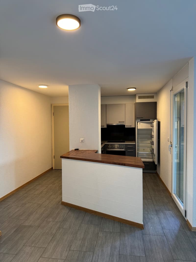 Modern kitchen with light-colored cabinets, stainless steel appliances, and a wooden countertop. The space features a tiled floor and recessed lighting.