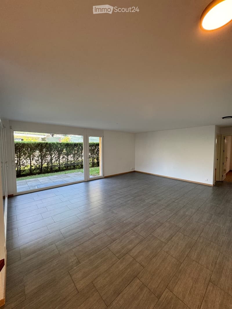 Empty room with wooden flooring, large sliding glass doors leading to a patio, and neutral-colored walls.
