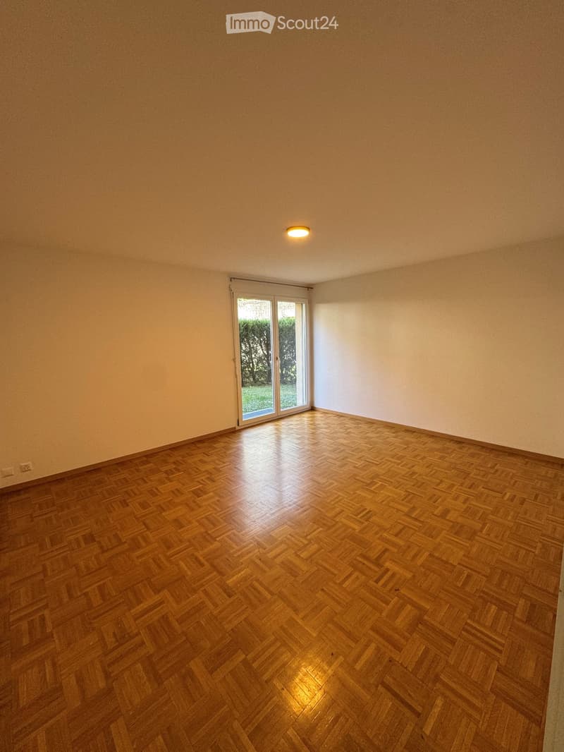 Empty room with wooden herringbone flooring, white walls, and a large sliding glass door leading to an outdoor area.