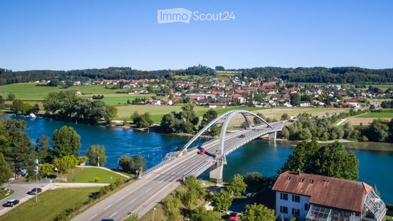 Aerial view of a town with a modern bridge over a river, surrounded by green fields and scattered houses.