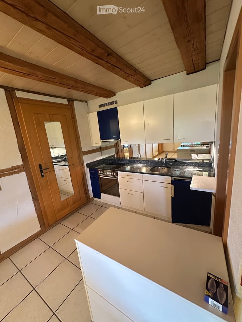 Modern kitchen with white cabinets, dark countertops, and stainless steel sink. Features an oven and a countertop island.