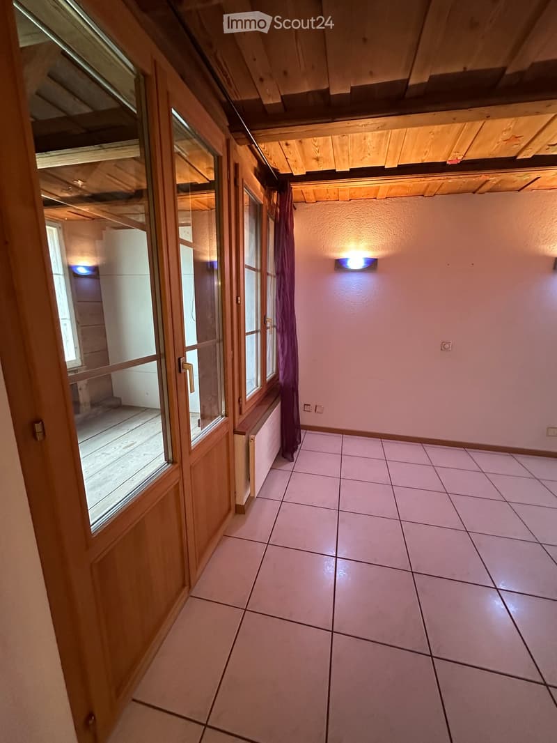 Empty hallway with tiled floor, wooden door, and exposed wooden beams on the ceiling.