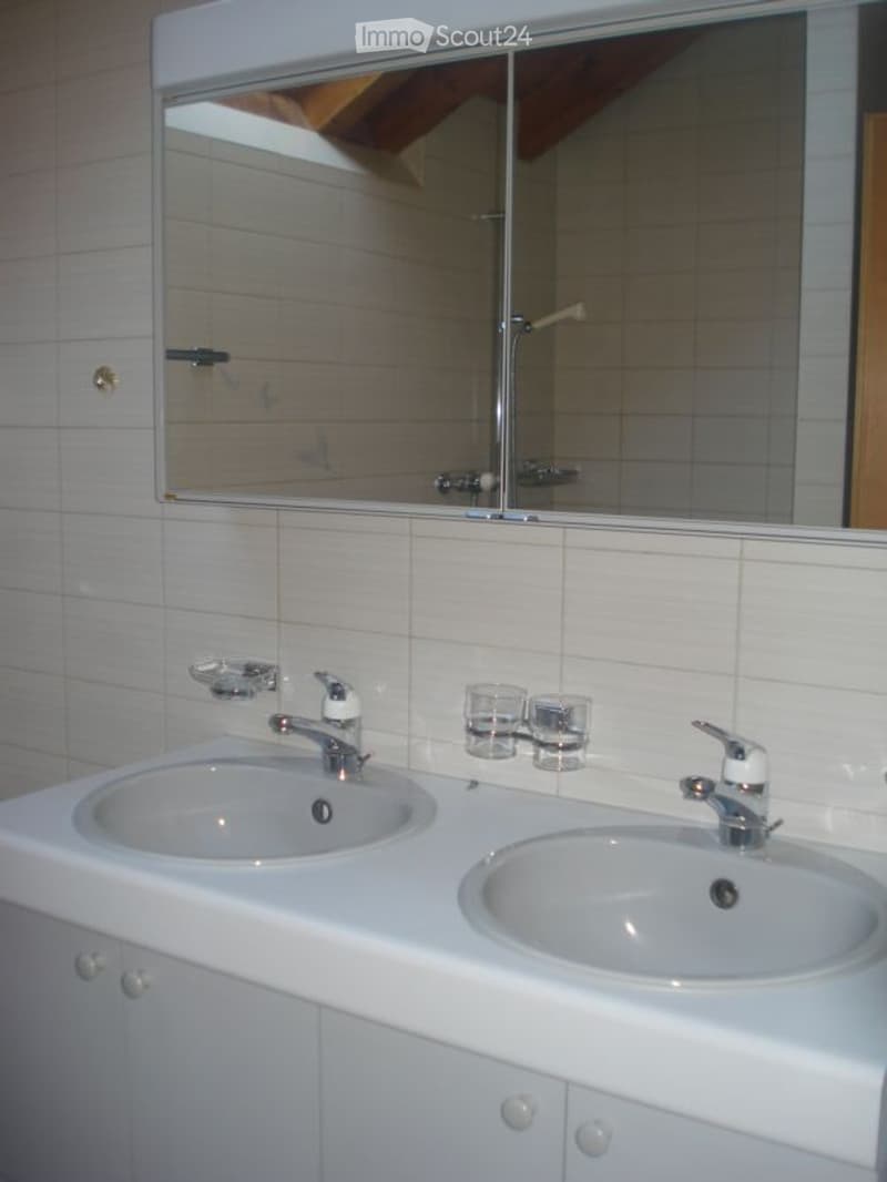 Modern bathroom with double sink vanity, white tiles, large mirror, and two cups on the counter.