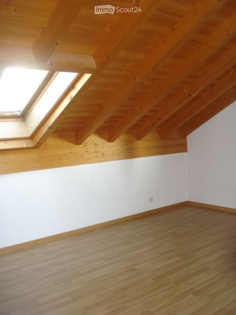 Empty room with wooden flooring and exposed wooden ceiling beams, featuring skylight windows allowing natural light.