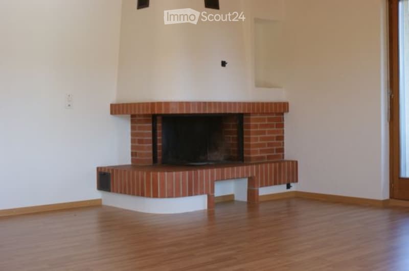 Empty room with wooden flooring and a brick fireplace against a white wall.