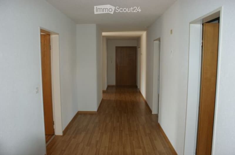 Empty hallway with wooden flooring and white walls, featuring several closed wooden doors on both sides.