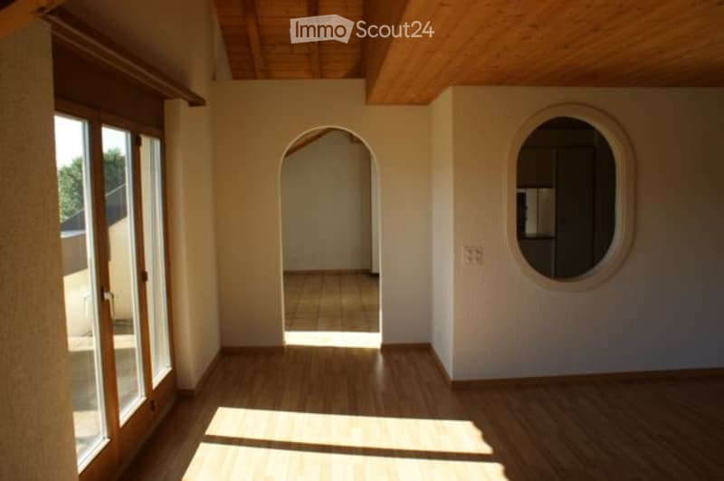 Empty room with wooden flooring, large windows, and an arched doorway leading to another space.