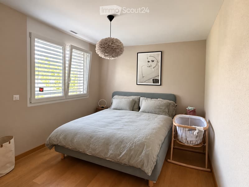 Cozy bedroom with a large bed, nightstand, baby crib, and decorative elements including a framed picture and a hanging decorative ball.