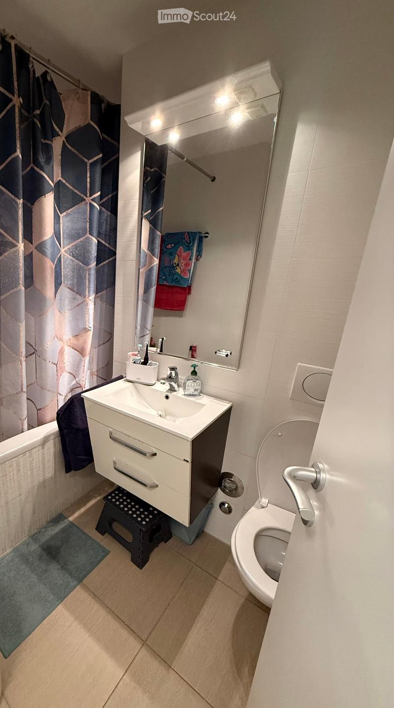 Modern bathroom with a white sink, toilet, mirror, and shower curtain. Includes a towel and a small cabinet under the sink.