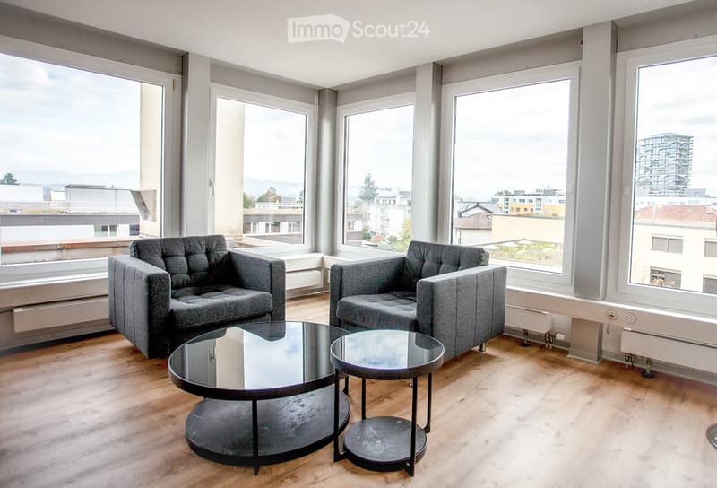 Modern living room with large windows offering a city view, featuring two grey sofas and a round glass coffee table.