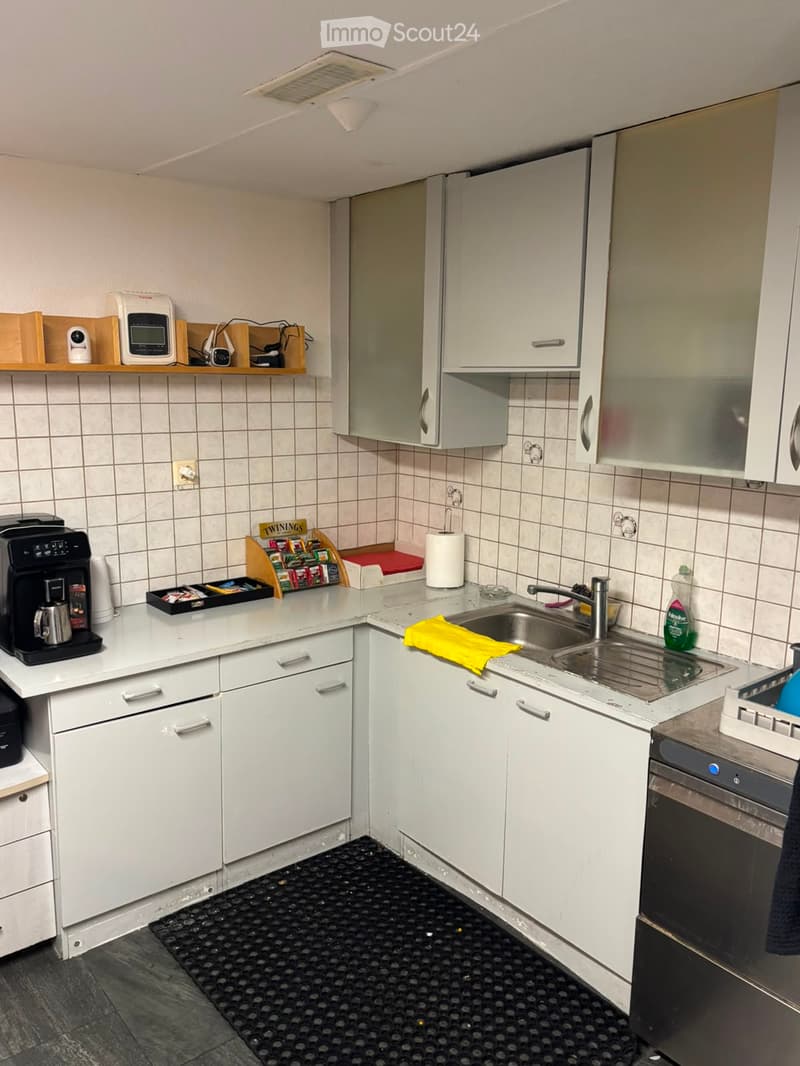 Modern kitchen with white cabinets, stainless steel appliances, and a double sink. Coffee maker, dish rack, and various small appliances are visible on the countertops.