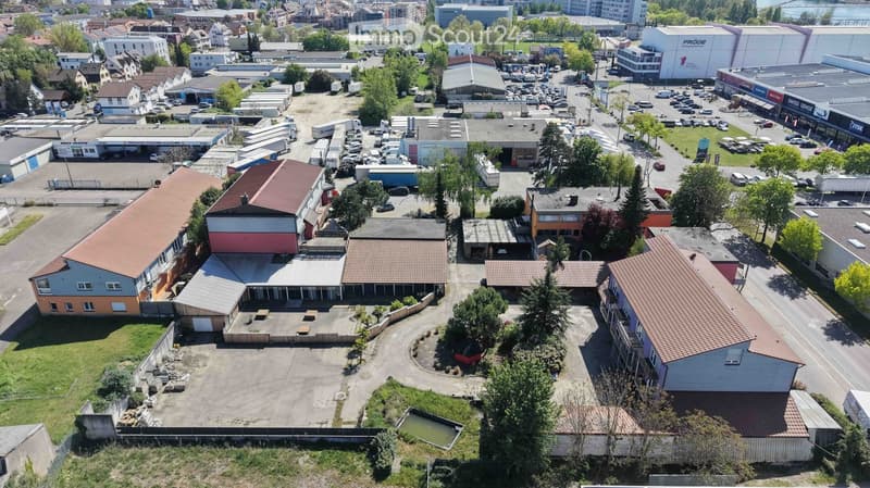 Aerial view of an industrial area with multiple buildings, parking lots, and surrounding greenery.