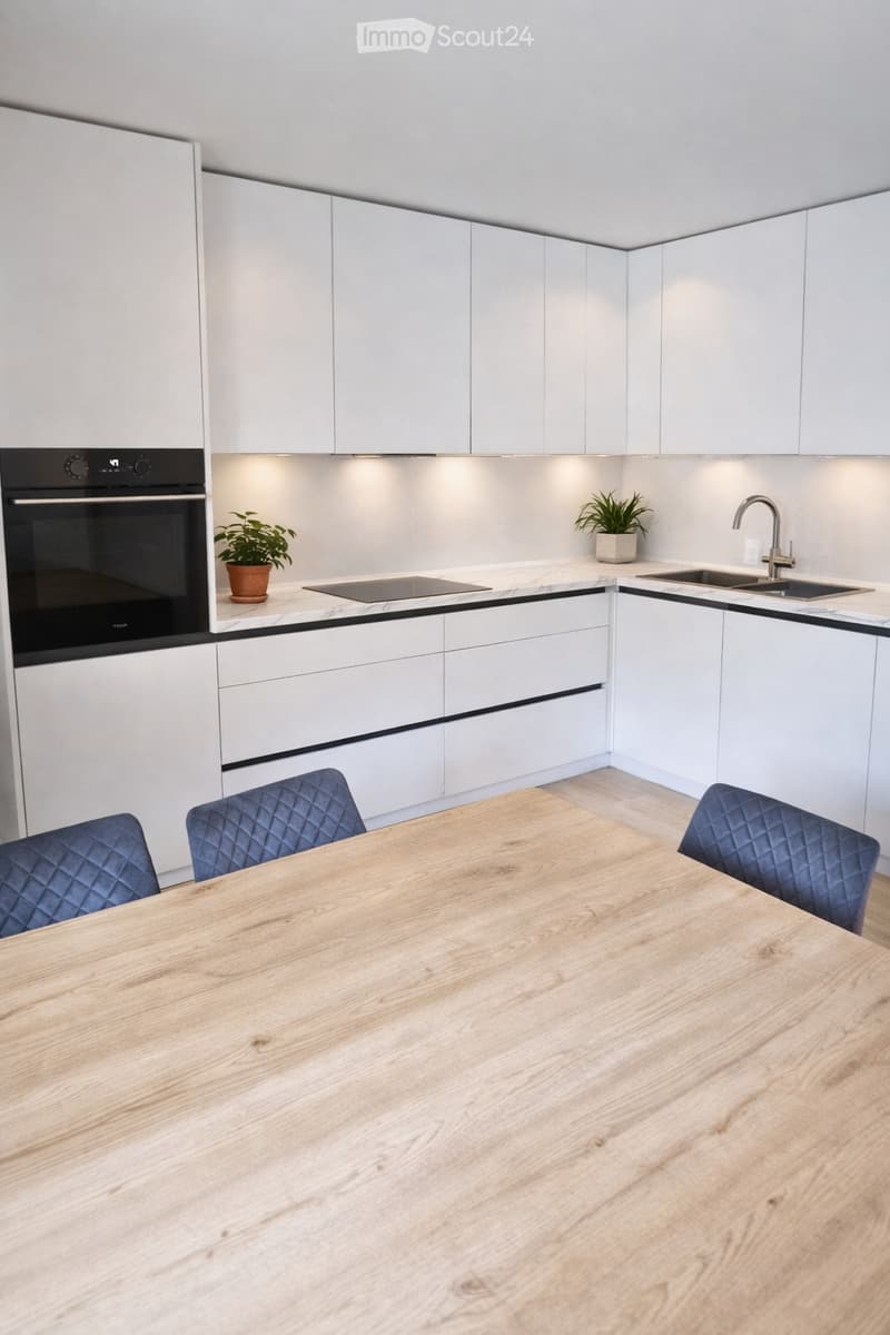 Modern kitchen with white cabinets, a wooden dining table, four blue chairs, a built-in oven, a sink with a modern faucet, and two small potted plants on the countertops.