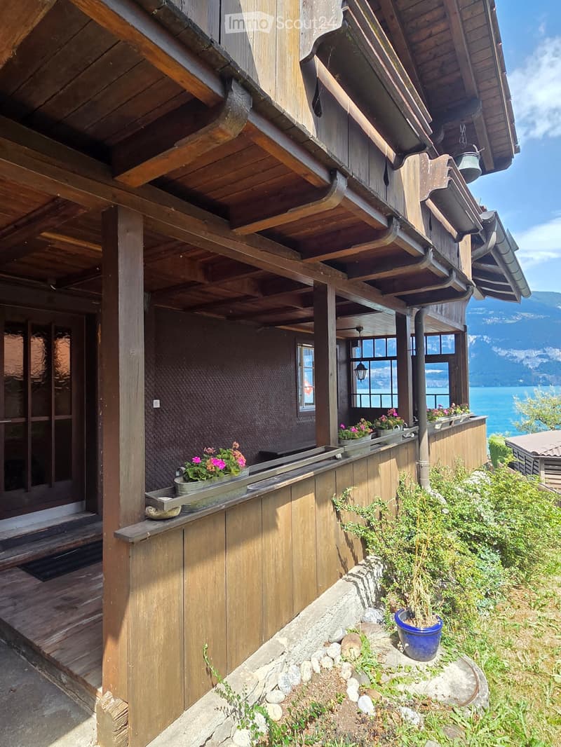 Wooden balcony with flower pots, overlooking a scenic lake and mountain view.