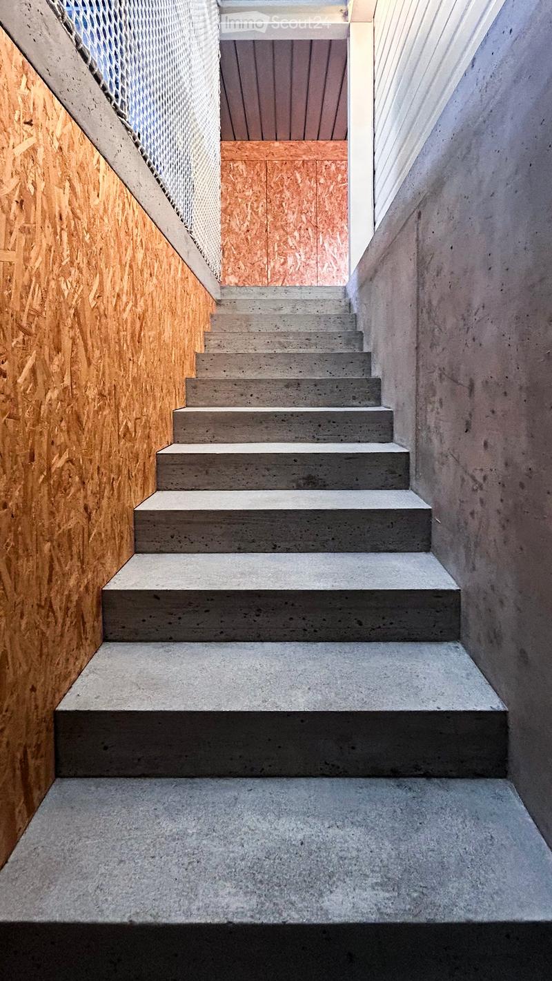 Concrete staircase with wooden paneling on one side and a metal mesh on the other, leading upwards.