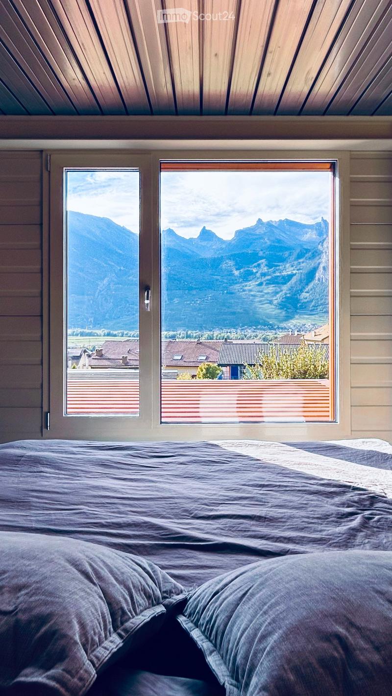 Bedroom with a large bed, pillows, and windows offering a scenic mountain view.