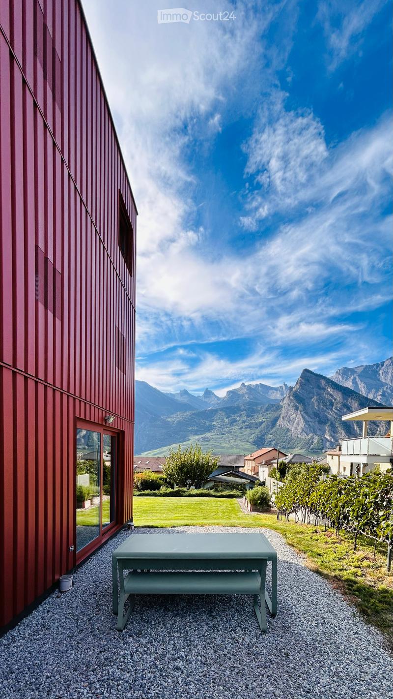 Outdoor patio area with a grey table, gravel flooring, and a view of mountains and vineyards.