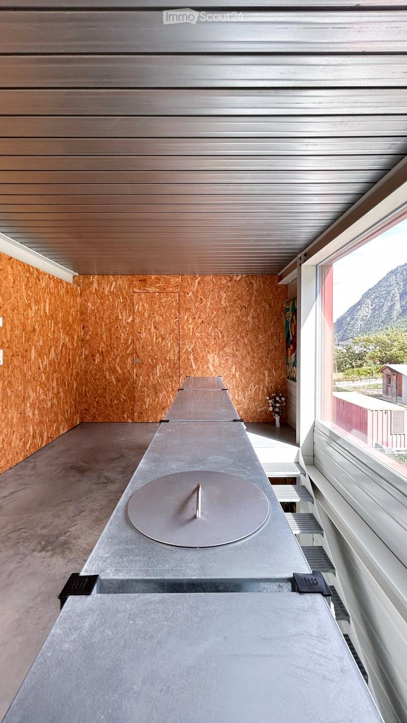 Modern balcony with wooden walls, large windows, and a concrete table with a round metal top.