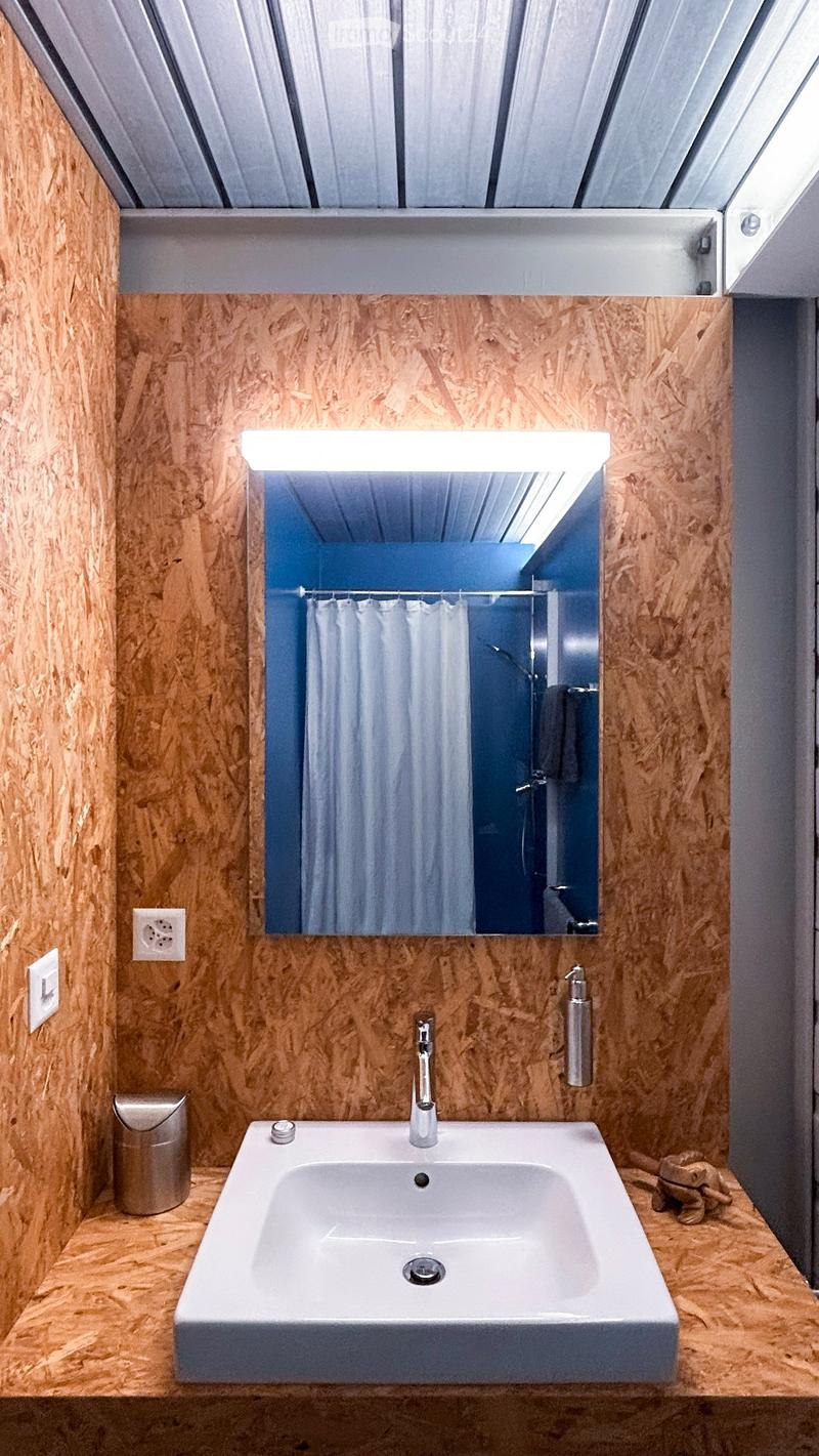 Modern bathroom with a white sink, chrome faucet, large mirror, and wooden panel walls.