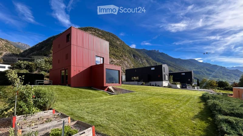 Modern red and black houses on a grassy lawn with mountain backdrop.