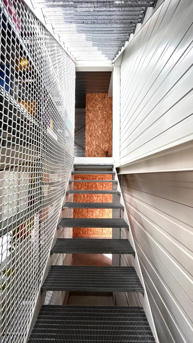 Modern staircase with metal steps and wooden risers, featuring a netted side wall and white paneling on the opposite side.
