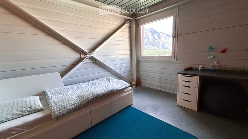 Cozy bedroom with a single bed, desk, and drawer unit. Large window offers a scenic mountain view.