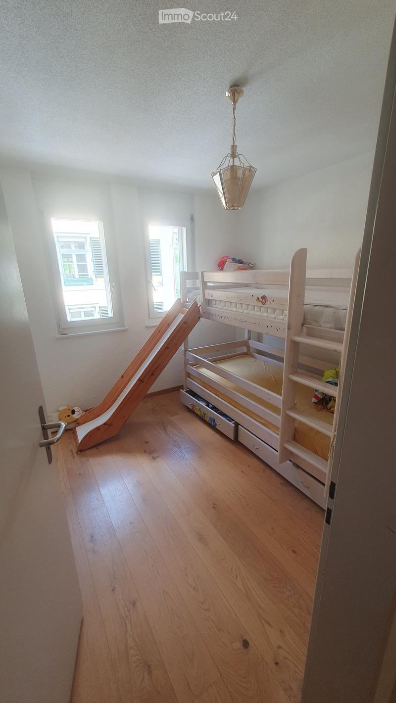 Bright bedroom with wooden floor, bunk bed with slide, drawers, and a small toy on the floor.