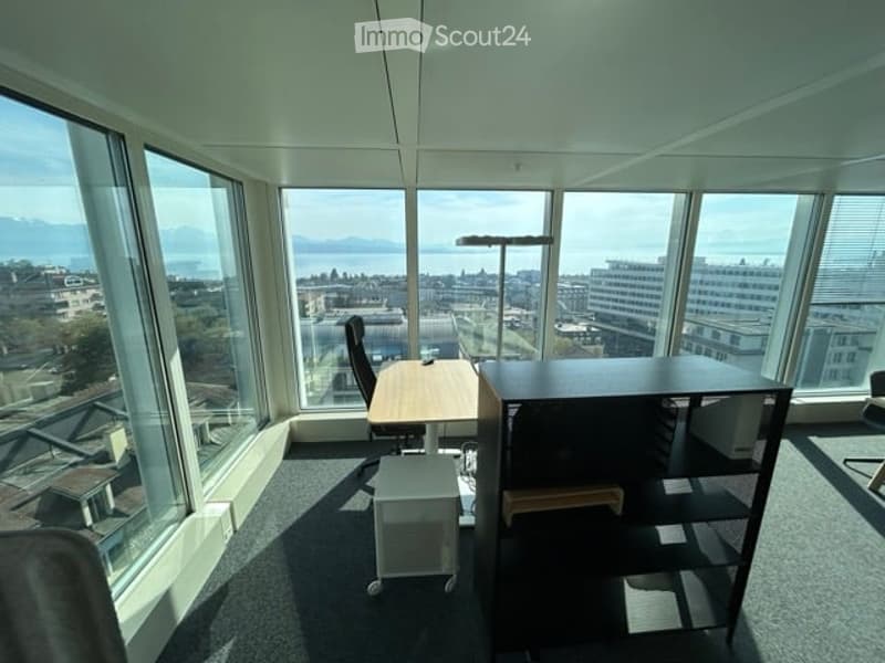 Bright office space with large windows offering a scenic city view, equipped with a desk, chair, and a floor lamp.
