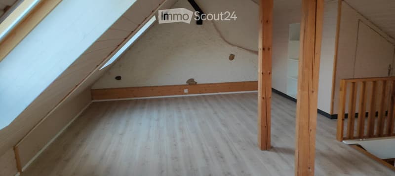 Empty attic space with wooden flooring, exposed wooden beams, and skylights allowing natural light.