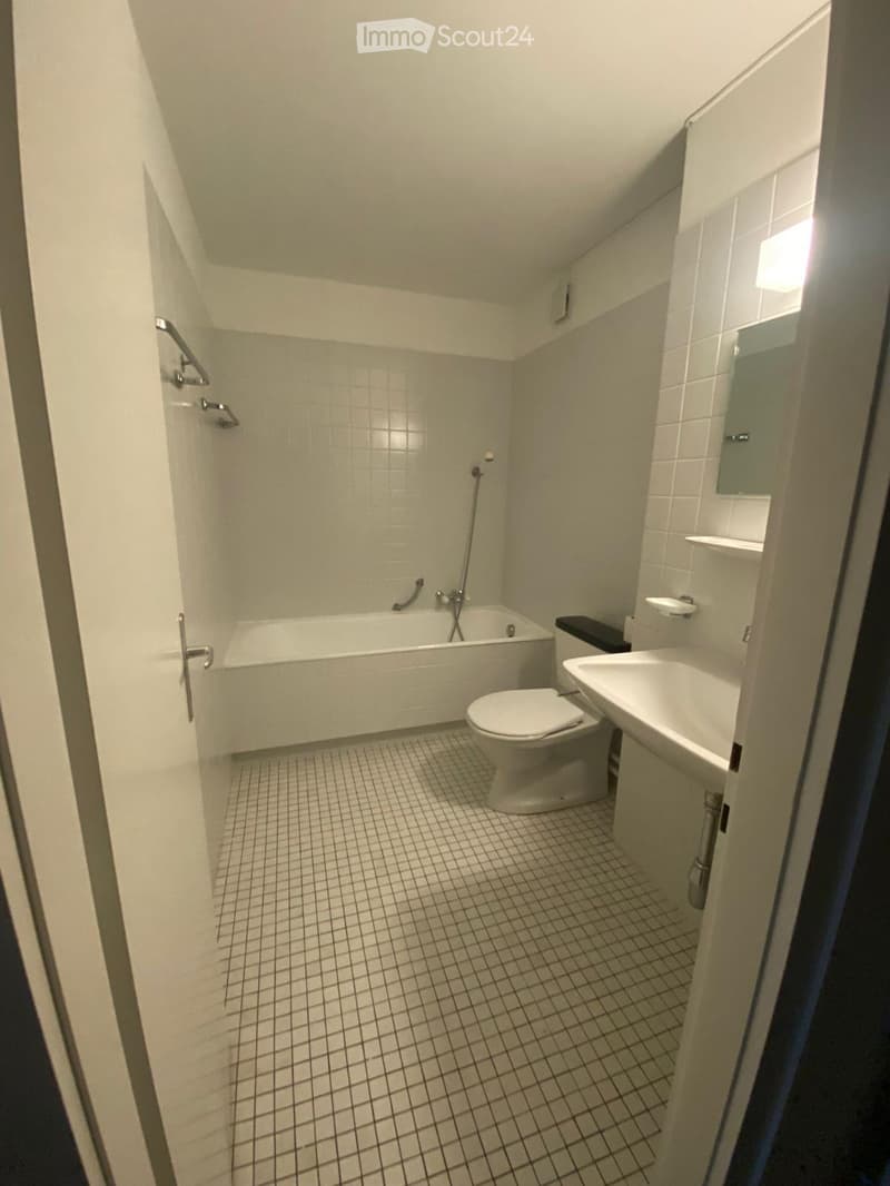 Modern bathroom with white tiled walls and floor, featuring a bathtub, toilet, sink, and mirror.