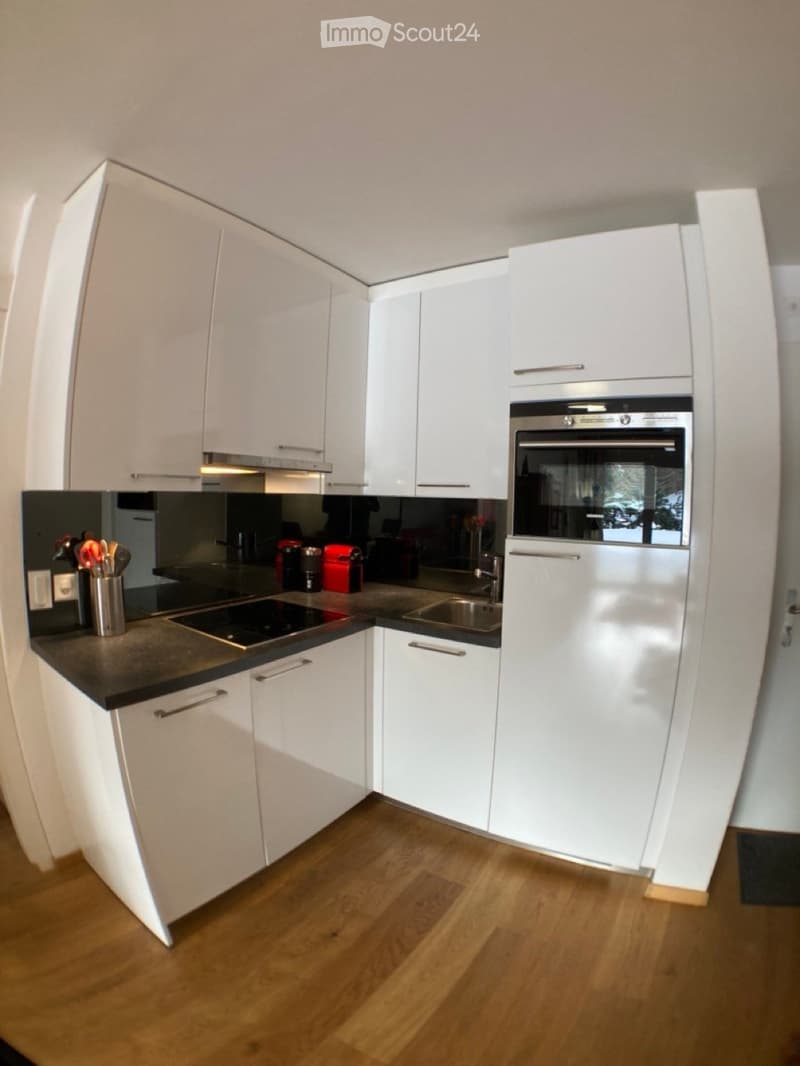 Modern kitchen with white cabinets, stainless steel oven, induction cooktop, and wooden flooring.
