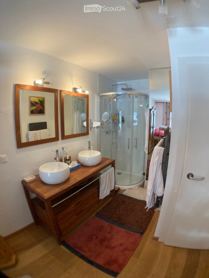 Modern bathroom with double sink vanity, large mirrors, glass shower enclosure, and towels.