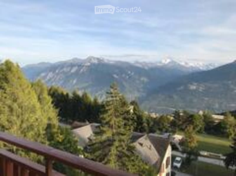 Balcony with wooden railing, overlooking a scenic mountain view and surrounding greenery.