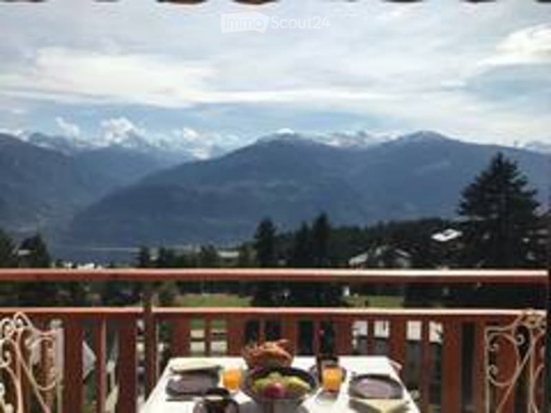 Balcony with a scenic mountain view, a table with a fruit bowl, and a cup.