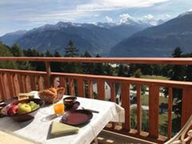 Balcony with a table set for breakfast, overlooking a mountain range with snow-capped peaks and a forested valley below.