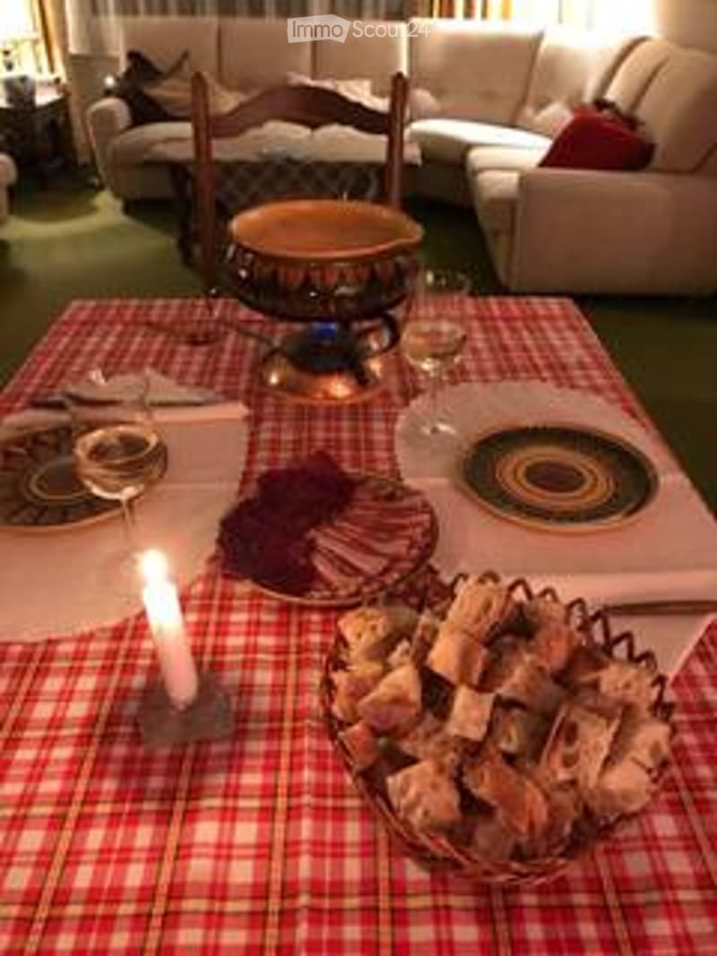 A dining area with a checkered tablecloth, plates, a candle, a bowl of food, and a sofa in the background.